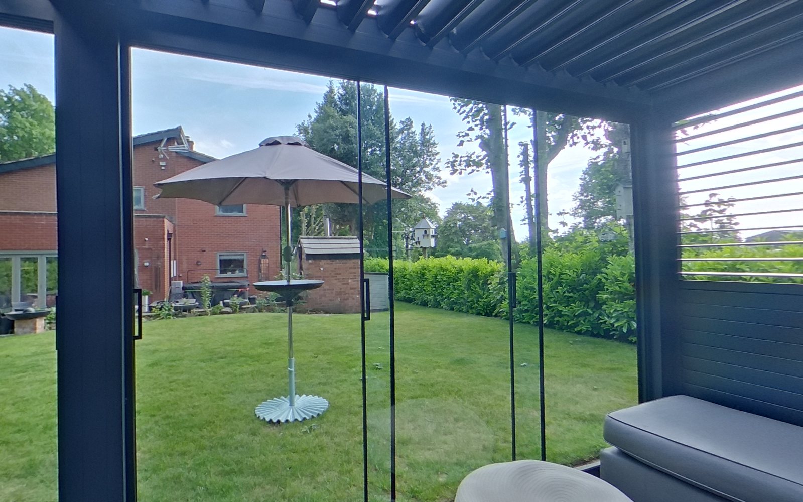 Looking out from the show pergola through its glass sliding sides to the lawn and house
