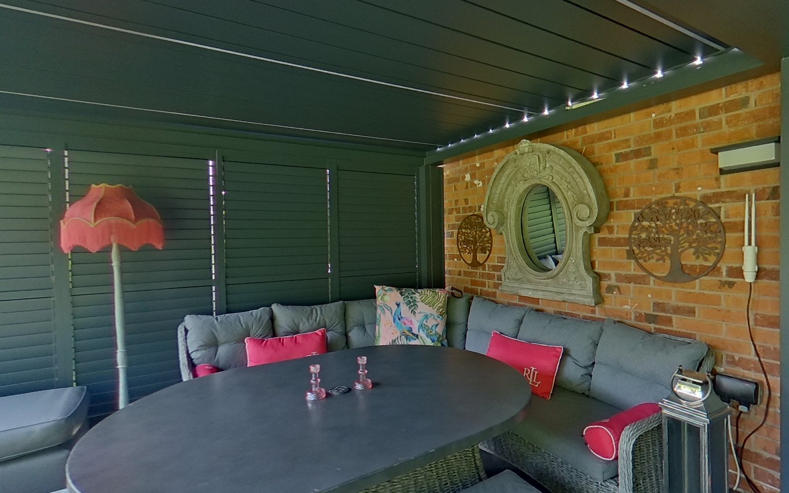 Inside the Pergola Pros show pergola at Retford: louvred roof closed, glass sliding sides, seating and dining area